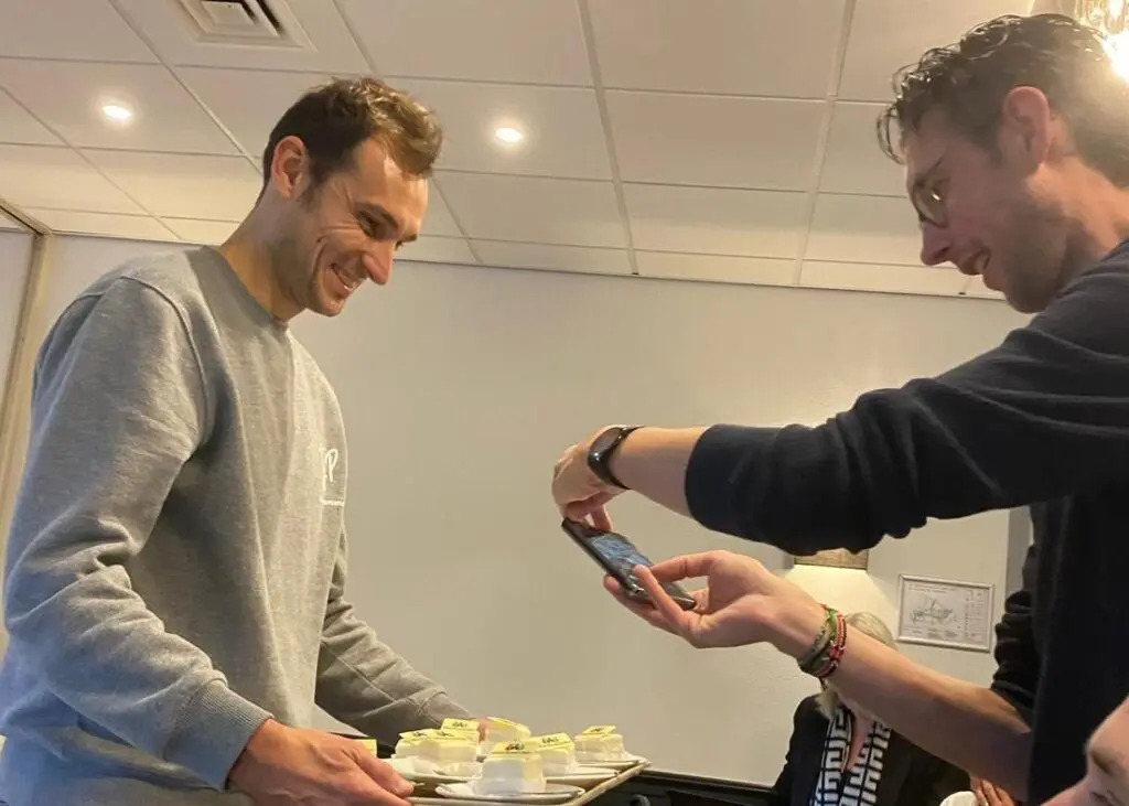 Kartrekkers van de nieuwe huisstijl van WeAreHR!, Simon Janssens en Joop van Diepen, bij de onthulling van het nieuwe logo van WeAreHR!. Zij delen taartjes uit aan de andere associates met daarop het nieuwe logo van WeAreHR!